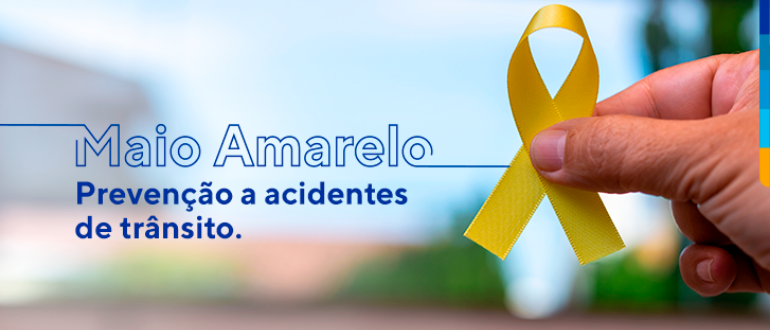 Maio Amarelo. Prevenção a acidentes de trânsito. Ao lado, m]ao masculina segurando laço amarelo