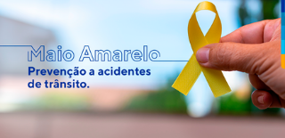 Maio Amarelo. Prevenção a acidentes de trânsito. Ao lado, m]ao masculina segurando laço amarelo