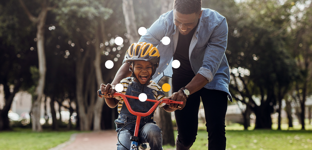 criança na bicicleta com o pai segurando, simbolizando proteção