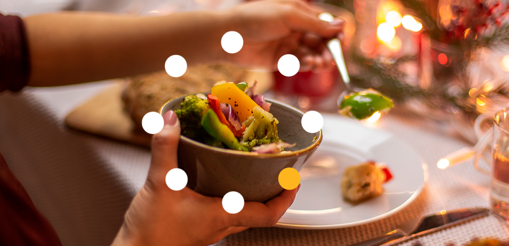 mãos segurando uma colher a na outra uma tigela com legumes, mesa com prato. simbolizando o equilíbrio nas festas de final de ano