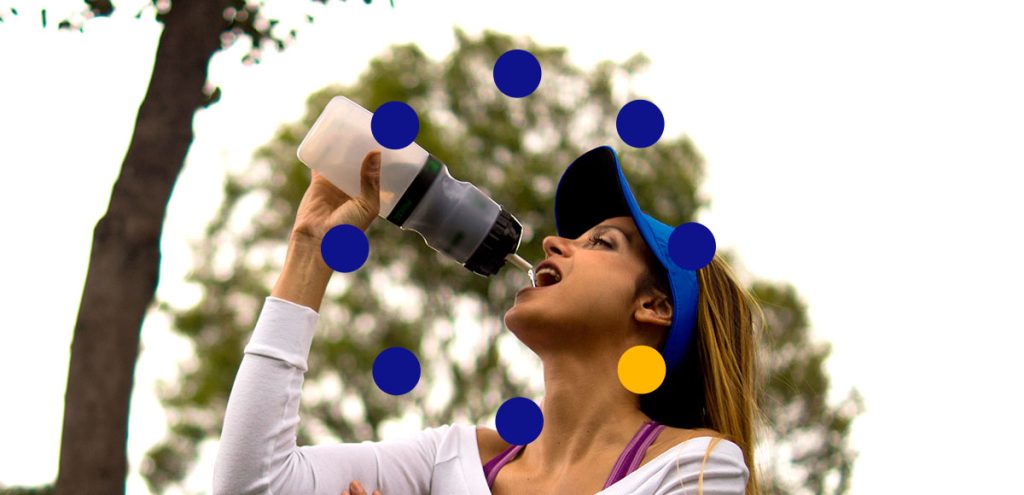 Mulher ao ar livre, com uma garrafa, tomando água, simbolizando atenção na prática de exercícios físicos em dias de temperaturas extremas no verão