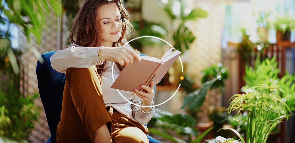 Mulher sentada numa cadeira em ambiente cheio de plantas um no seu momento de leitura, simbolizando hábitos para melhorar a memória