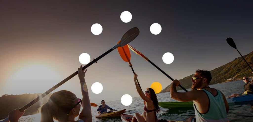 grupo de amigos dentro de alguns caiaques em alto mar com os remos para cima, simbolizando 10 ideias de esportes para praticar no verão