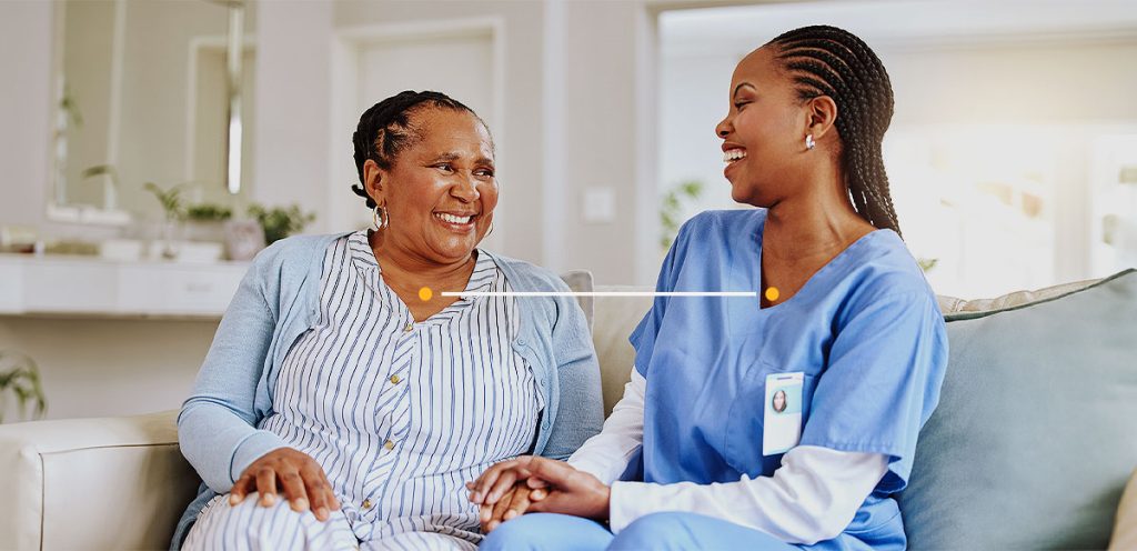 a imagem possui duas mulheres sentada em um sofá, sendo uma médica dando informações sobre saúde da mulher para sua paciente.