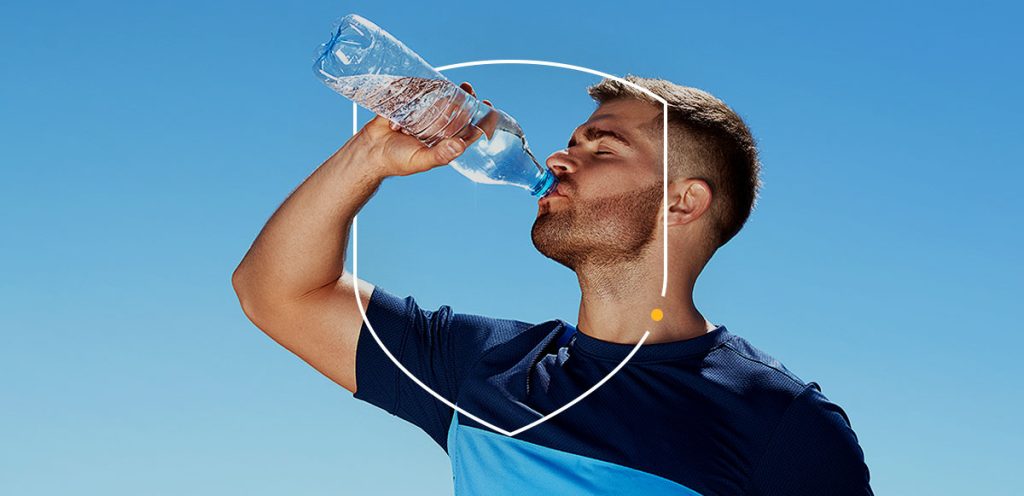 Imagem de um rapaz tomando água em uma garrafa durante um dia ensolarado. Simbolizando dicas para manter a saúde em meio às mudanças climáticas.