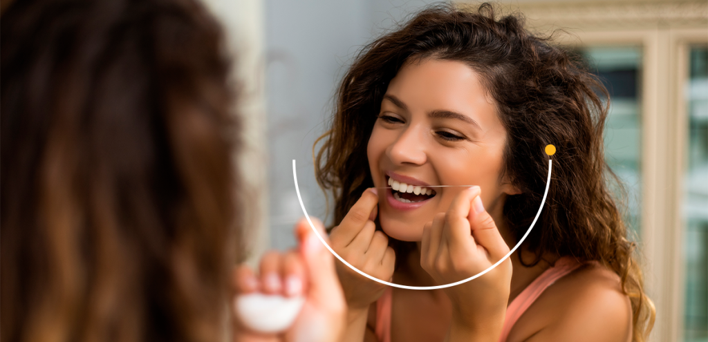 Imagem de uma mulher passando fio dental para representar: Por que cuidar da saúde bucal influencia o corpo todo