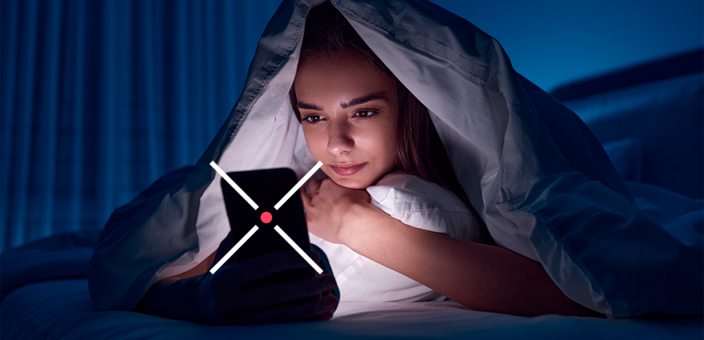Imagem de uma mulher deitada na cama mexendo no celular para representar: X hábitos noturnos que afetam sua saúde