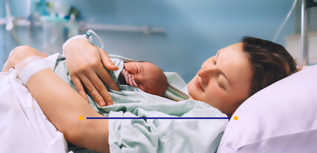 Imagem de uma mulher segurando uma criança após o parto em um leito de hospital, simbolizando o puerpério