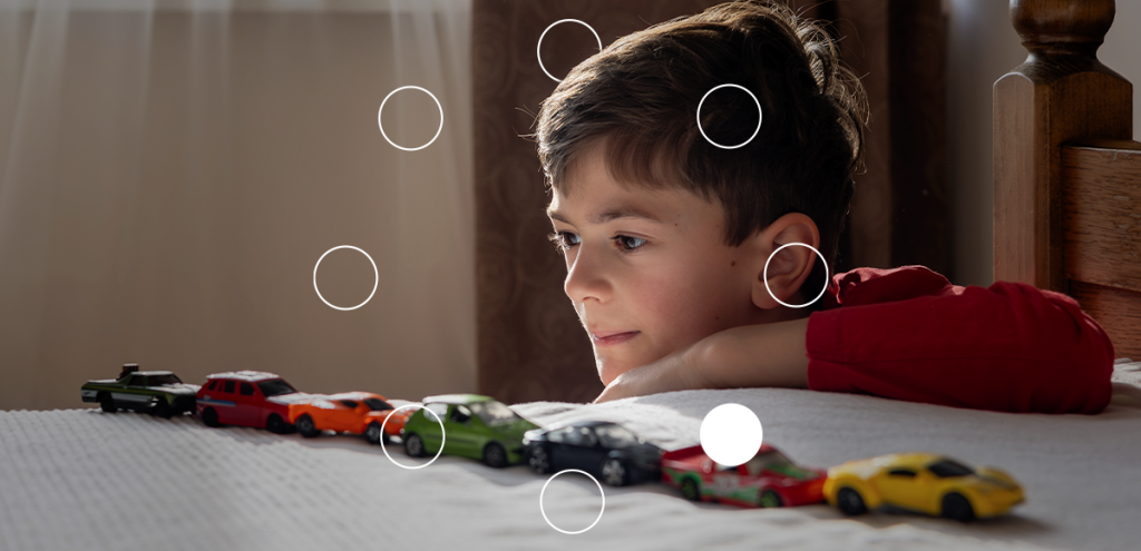 Criança pequena observando carrinhos enfileirados, ilustração comum usada para exemplificar sinais precoces do autismo relacionados à brincadeira repetitiva e atenção focada.