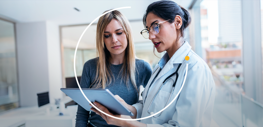 Médica especialista mostrando exames em um tablet para paciente, destacando o diagnóstico e a importância do acompanhamento em consulta de saúde.