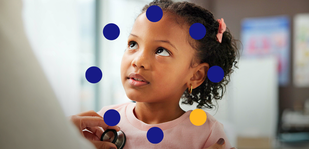 O momento de um exame pediátrico, onde uma menina olha para cima com expressão curiosa enquanto um médico ou enfermeiro escuta seu coração com um estetoscópio.