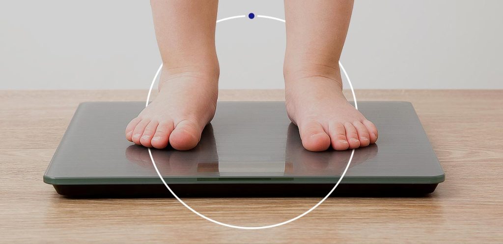 Imagem de pés de uma criança em cima de uma balança, simbolizando obesidade infantil